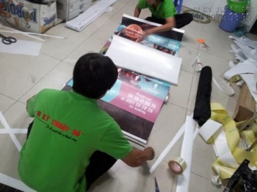 Nhân viên gia công đang lắp poster vào banner cuốn cho khách hàng